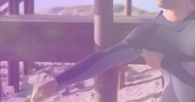 Tahta iskelenin altında duran sörfçü neoprene dalgıç kıyafetiyle su sporlarına hazırlanıyor. Macera, sahil, açık hava, spor, aktivite, eğlence, çok yönlülük