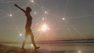 Güneş doğarken, siluet yürüyen kadın kıyı şeridini başlatırken ağ titreşimleri teknolojiyi gösteriyor. Şafak, ufuk, bağlantı, dinginlik, yenilik, siluet, yansıma