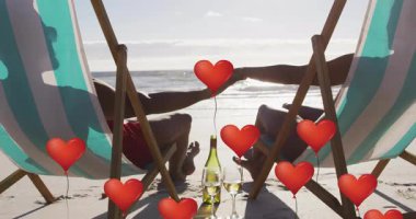Güneşli sahilde sandalyede oturan çift romantik reklamlar için kırmızı kalp balonlarının yükselmesine neden oluyor. Romantizm, şefkat, huzur, samimiyet, rahatlık, sahil, sükunet.