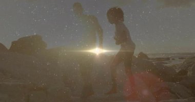 Çift kayaların üzerinde yürürken, güneş gözlüğünü çıkarırken ve seyahat titreşimlerini uyandırırken güneş mercekleri parlıyor. Romantizm, siluet, günbatımı, macera, sahil, bağlantı, sükunet