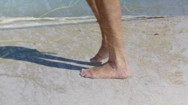 Sağlıklı olmak için güneşli sahilde çıplak ayakla yürüyen ıslak kuma basıp ayak izleri bırakan bir kadın. Plaj, yalınayak, kıyı şeridi, kum, okyanus, dalgalar, ayak sesleri