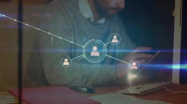 Teknoloji masasındaki akıllı telefonları dinleyen ve yazan adam çalışma alanı boyunca genişleyen kullanıcı simgelerini izliyor. Teknoloji, ağ oluşturma, dijital, yenilik, bağlantı, çalışma alanı, modern