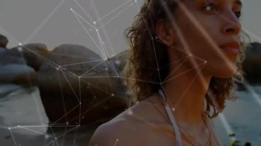 Gün batımında kayalık kıyıda duran bir kadın, kayışı koruyan bir eş, sürüklenen teknoloji hatları, yükselen alevler. Dijital, dinginlik, zarafet, açık hava, manzara, refah, modern