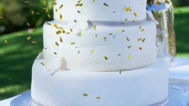 Altın konfeti, üç katlı beyaz düğün pastasının üzerine yağıyor. Çiçekler ve Bay ve Bayan Topper 'ı gösteriyor. Kutlama, zarafet, taşra, coşku, neşe, sofistike, yeşillik