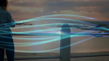 Elinde akıllı telefon tutan bir kadın trabzanda cep telefonu görüşmesi yapıyor. Ufukta titreyen neon çizgiler var. Dijital, sükunet, rahatlık, modern, manzaralı, çevresel, düşünceli