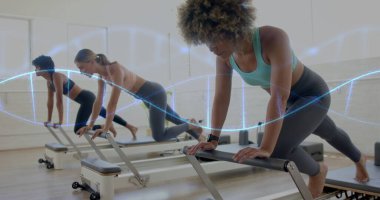 Leaning three women holding knee plank on reformer machines in bright Pilates studio, with trackers. Fitness, wellness, workout, strength, active, health, exercise