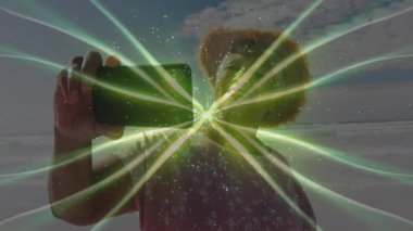 Üst düzey kadın kıyıda akıllı telefon tutuyor ve sosyal medya için yeşil fraktal dalga filtresini çalıştırıyor. Dijital sanat, yaratıcılık, dinginlik, açık hava, canlı, teknoloji, farkındalık