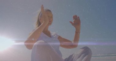 Sahilde kollarını kaldıran, dua eden yaşlı bir kadın, merceğin alevi arasında refah pozu veriyor. Dinginlik, farkındalık, sükunet, ruhsal rahatlama, doğa, meditasyon.