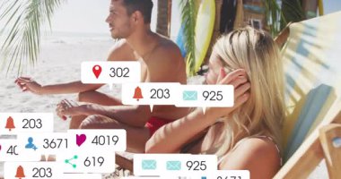 Plaj sandalyesinde oturan ve kollarını uzatan bir çift, pazarlama için çevrelerine sosyal simgeler yerleştiriyor. Tatil, boş zaman, açık hava, yaşam tarzı, dijital bağlantı, rahatlama