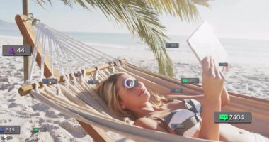 Plaj hamağında tablet görüntüleme simgesiyle uzanan flama, baloncuklar gibi sohbeti gösteriyor. Açık hava, rahatlama, dijital etki, yaşam tarzı, tropikal, teknoloji