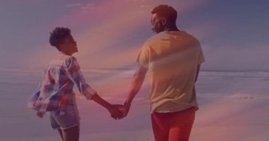 Gün batımı kumsalında el ele tutuşan gezgin çift, dalgalar dönerken işaret eden kadın. Romantizm, arkadaşlık, deniz kenarı, sükunet, macera, sükunet, beraberlik.