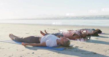 Sahilde yoga yapan dört kadın sosyal medya simgeleriyle güncel ve solgun görünüyor. Dinginlik, sağlık, farkındalık, açık hava, doğal ortam, sosyal ilişki, dijital etkileşim