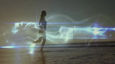 Orta yaşlı bir kadın deniz suyunda gün batımına doğru yürüyor, sağlık her tekmede titreşen ışık ile örtüşüyor. Plaj, gün batımı, yansıma, dinginlik, hareket, dijital efektler, sağlık