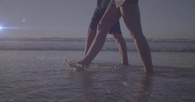 Çift sörf yapmak ve ıslak kumda çıplak ayakla yürümek Pastel gökyüzünün altında seyahat görsellerini gösteriyor. Sahil, sahil, dinginlik, rahatlık, romantizm, çevre, doğa.