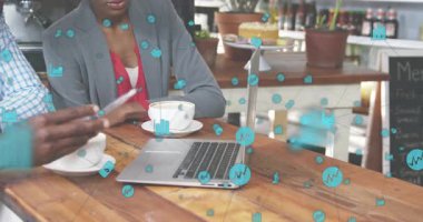 Kadın kahve fincanı yerleştiriyor ve erkek masaya oturuyor. Ekranda dönen simgelerle verileri analiz ediyor. İşbirliği, takım çalışması, analitik, modern, iş dünyası, başlangıç, yenilik