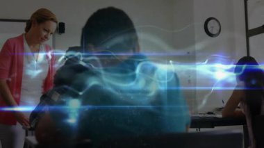 Öğretmen, yazı yazan öğrencinin üzerine eğilip, masalarda dönen mavi enerjiyi çalıştırarak, öğrenmeyi yönlendiriyor. Eğitim, sınıf, öğrenim, akıl hocalığı, konsantrasyon, yenilik, ilham