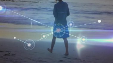 Alacakaranlıkta ıslak kuma basan bir kadın dijital ağ düğümlerini etkinleştiriyor ve teknoloji bağlantılarını gösteriyor. Deniz kıyısı, gün batımı, bağlantı, yenilik, dinginlik, gelecekçilik, zarafet.