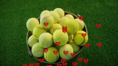 Bir saniye içinde, yeşil alanda sarı tenis toplarını tutan kovada dönen kırmızı kalpler üst üste biniyor. Spor, neşeli, enerjik, dinamik, neşeli, animasyon, eğlence
