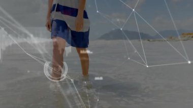 Adam sığ sulara adım atıyor ve teknoloji ağları sürüklenirken kıyı şeridi boyunca yürüyor. Sahil, sahil, kıyı şeridi, su, dalgalar, sandal ağacı, dijital