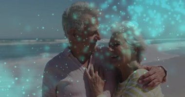 Seyahat reklamı için kıyı şeridini kucaklayan ve sürüklenen mavimsi parçacıkları renklendiren bir çift. Romantizm, arkadaşlık, dinginlik, okyanus manzarası, sükunet, kutlama, canlılık