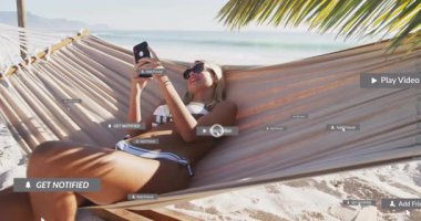 Kumsalda hamakta uzanan bir kadın akıllı telefonları nazikçe dinliyor ve sosyal medya alarmlarını çalıştırıyor. Tropikal, boş zaman, yaz tatili, rahatlama, teknoloji, kaçış, açık hava