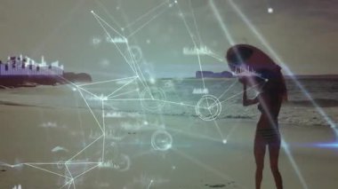 Sörf tahtası taşıyan bir kadın kumda yürüyor ve teknoloji gösterisi için kaplamayı etkinleştiriyor. Plaj, okyanus, dalgalar, dijital, bağlantı, teknoloji, huzur