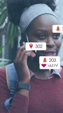 Animation of multiple social media icons over african american woman talking on smartphone outdoors. Social media networking and technology concept