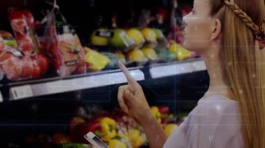 Bakkal reyonunda telefon dinleyen bir kadın, hareketli fiyat etiketleri gösteren, tazelik için biberleri kontrol eden bir kadın. Alışveriş, tazelik, teknoloji, tüketici, tarım, sağlıklı, perakende