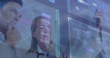 Kıdemli hekim ve meslektaşım laboratuarda dijital ekranda çizelgeleri inceliyor, laboratuvar önlükleri giyiyorlar. Tıbbi, işbirliği, geleceksel, yenilik, araştırma, analiz, sağlık