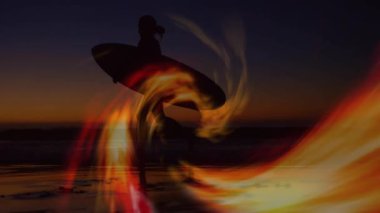 Kıvrımlı kırmızı-sarı kurdeleli, kıyıya yürüyen sörfçü, pazarlama için iz sürme tahtası. Siluet, sahil, okyanus, günbatımı, ışık yolları, iz sürme efektleri, macera