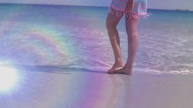 Kadın sörf yapıyor, sahil şeridinde yürüyor ve seyahat pazarında eğlenceli sıçramalar yaratıyor. Sahil, kıyı şeridi, okyanus, ayak izleri, su, güneş ışığı, boş zaman