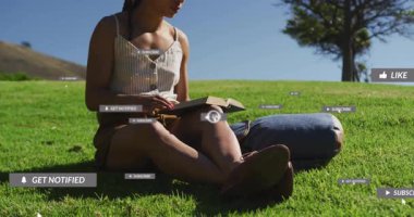 Çimenler üzerine kitap okuyan bir kadın imlecin sosyal bildirimleri yöneten ikonlar gibi tıklamasını izliyor. Doğa, rahatlama, dijital arayüz, farkındalık, açık hava, boş zaman, minimalizm