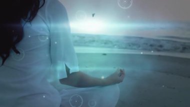 Gün doğumunda sahilde meditasyon yapan bir kadın parlak küreler yaratıyor ve meditasyon uygulaması için örtüyor. Dinginlik, farkındalık, dijital alarm, sükunet, sağlık, ruhsal, atmosferik