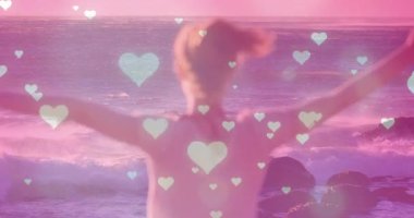 Kayalık sahilde bir kadın, gün batımında dalgalar yükselen kollar, sağlık pazarlaması için yüzen kalpler. Romantik, dinginlik, ahenk, sağIık, sükunet, doğal, canlı
