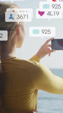 Deniz yoluyla fotoğraf çeken çift, sosyal medya bilgilendirmeleriyle çevrili. Tatil, plaj, romantizm, akıllı telefon, internet, deniz kenarı