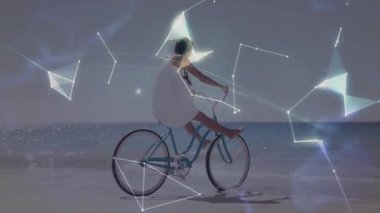 Sahil şeridinde bisiklet süren bir kadın ağ teknolojisini etkinleştiriyor ve holografik küreyi şekillendiriyor. Yaşam tarzı, dijital alarm, gelecekçi, okyanus, teknoloji, macera, manzara
