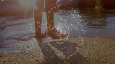 Adam gün batımında kumdan deniz suyuna adım atarak dönen teknoloji küresini gösteriyor. Sahil, teknoloji, fütüristik, minimalist, yenilik, huzur, soyut