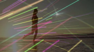 Kadın kumda suya girip tekmeliyor, seyahat pazarlaması için animasyon ışık çizgilerini aktifleştiriyor. Plaj, gün batımı, siluet, hareket, soyut, canlı, dinginlik