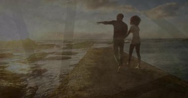 Gün batımında yürüyen bir çift, okyanus ufkunu gösteren kolunu kaldıran bir adam, seyahat reklamı için geri dönüyorlar. Aşk, siluet, manzara, ufuk, sükunet, bağlantı, macera