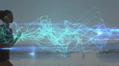 Neon sağlık dalgaları tempo ritmiyle senkronize olurken bir kadın kareye giriyor ve sahile doğru koşuyor. Zindelik, zindelik, enerji, dijital, canlı, hareket, açık hava