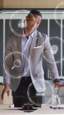 Afro-Amerikan iş adamının ofisindeki dijital simgelerin animasyonu. Küresel finans, iş, bağlantılar, hesaplama ve veri işleme kavramı dijital olarak oluşturulmuş video.