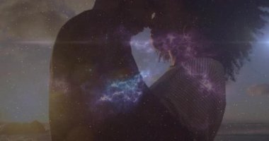 Günbatımı plajında alnına yaslanan erkek ve kadın, teknoloji alanında nebula kıvılcımları saçıyor ve birbirlerine bağlanıyorlar. Romantizm, samimiyet, siluet, kozmik, birlik, uyum, günbatımı