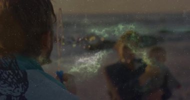 Lifestyle beach showing man dipping wand and blowing green bubbles drifting and entertaining child. Family, leisure, joyful, serene, pastel, vibrant, playful