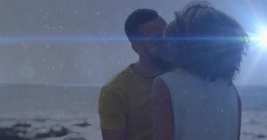 Seated couple turning and smiling sparking light particles and lens flare before kiss in film. Romance, intimacy, affectionate, relaxation, sunset, seaside, candid