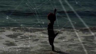 Kadın dalgaların içinden geçiyor, zıplıyor, su sıçrıyor ve ufukta geziniyor. Teknoloji parıldıyor. Siluet, okyanus, sahil, hareket, dijital, soyut, kıyı şeridi