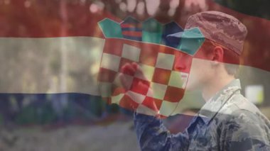 Hizmet üyesi, Hırvat bayrağıyla askeri bayrağını indirirken el pençe divan selam veriyor. Vatanseverlik, disiplin, onur, tören, açık hava, yeşillik, resmi