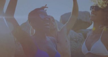 Seyahat güneşi, gün batımını kutlayan plajda dans eden ve kollarını kaldıran üç arkadaşa kıvılcım saçıyor. Sahil, sahil, arkadaşlık, açık hava, kutlama, eğlence, coşku