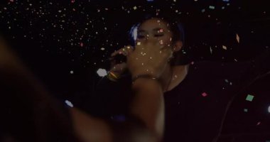 Konser şarkıcısı arka planda şarkı söylerken hayranlar onlara uzanıp yakınlaşırken konfeti ateşliyor. Performans, eğlence, kutlama, canlı, dinamik, bağlantı, alkış