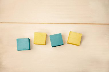 Düz dizayn ahşap yüzeyde dört tahta bloğu gösteriyor, gök mavisi ve sarıyı renklendiriyor. Minimalist, modern, geometrik, zanaat, doğal, nötr, renkli