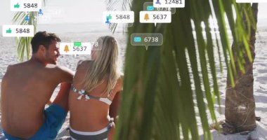 Avuç içlerine yaslanmış sosyal medya simgelerini ateşleyen sohbet eden çiftler etraflarında kümeleniyorlar. Tropikal, boş zaman, romantizm, dijital, gevşeme, canlı, dingin